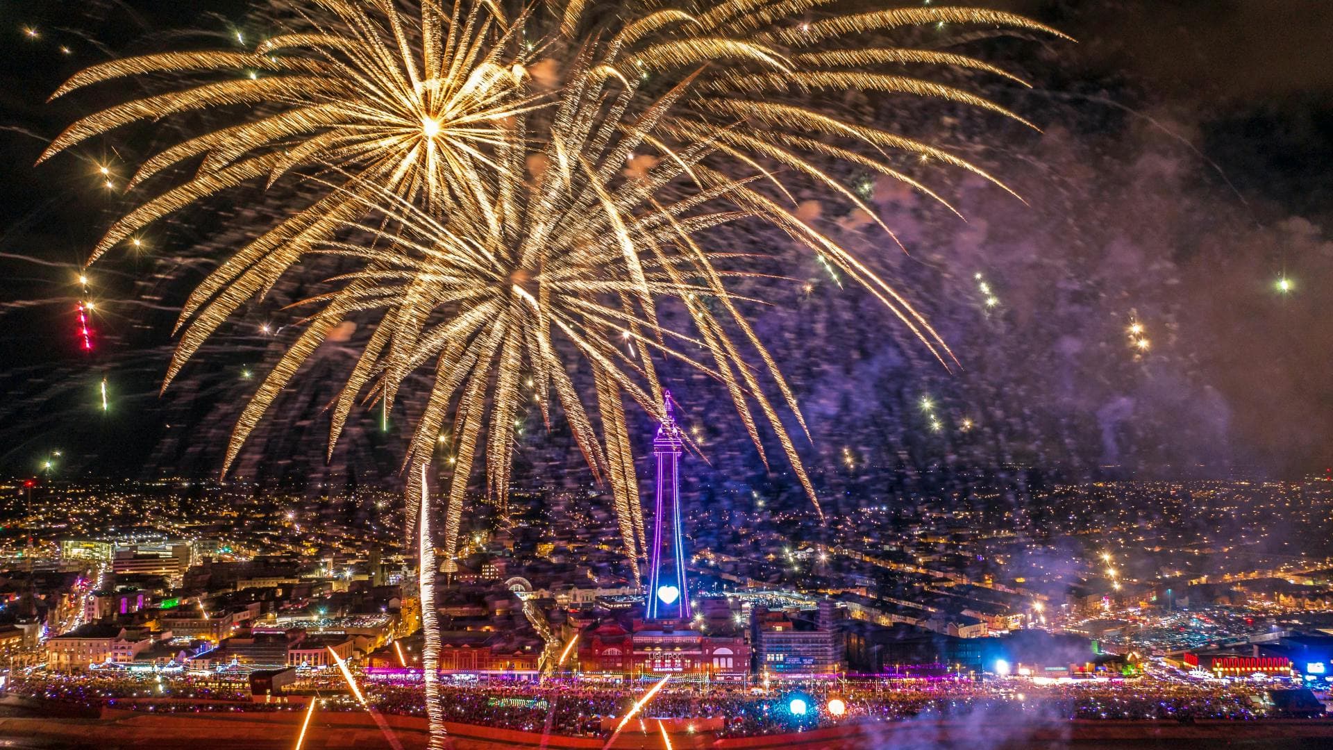 Fireworks display at night over a city with a tall tower.