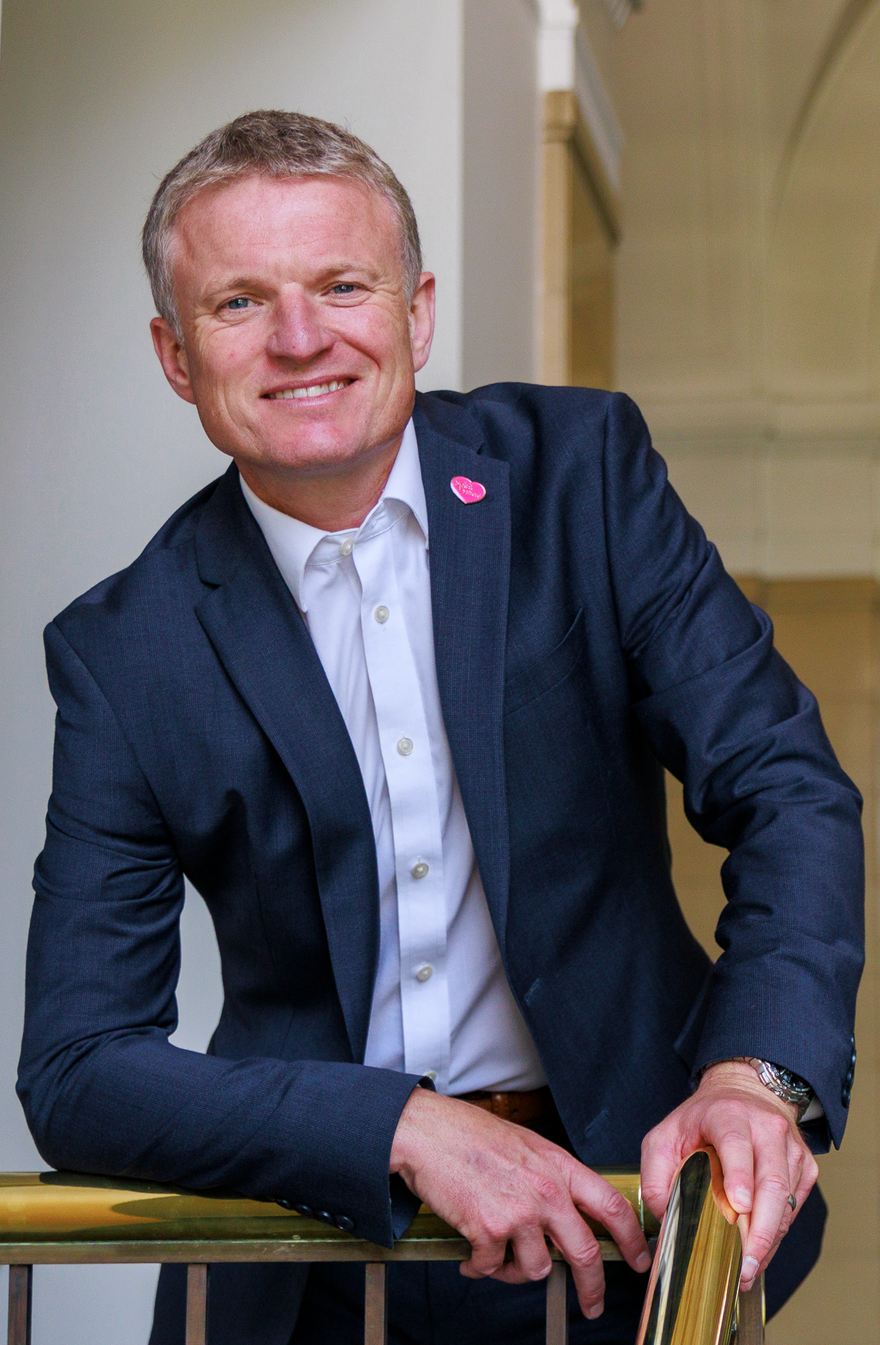 Man in a suit smiling, leaning on a railing.