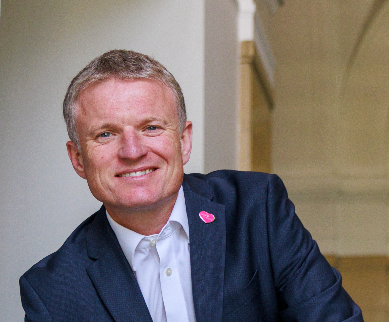 Man in a suit smiling, leaning on a railing.