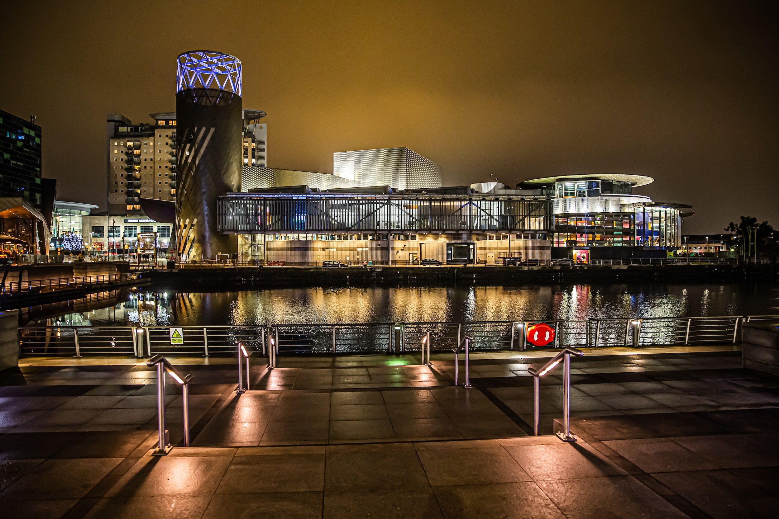 Buildings lit up at night, reflecting in the water.