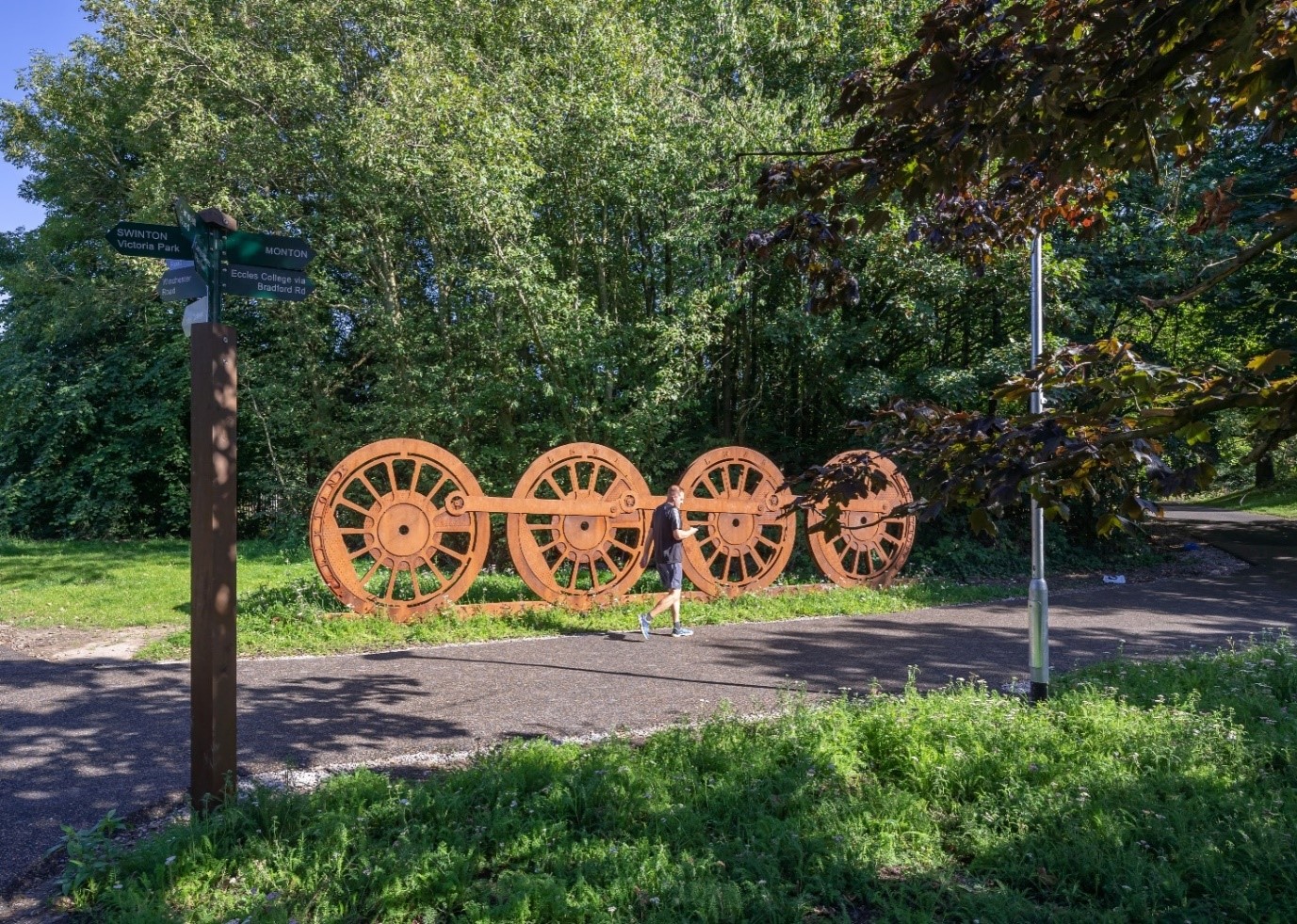 Rusty metal train wheels on the pathway with a runner walking.