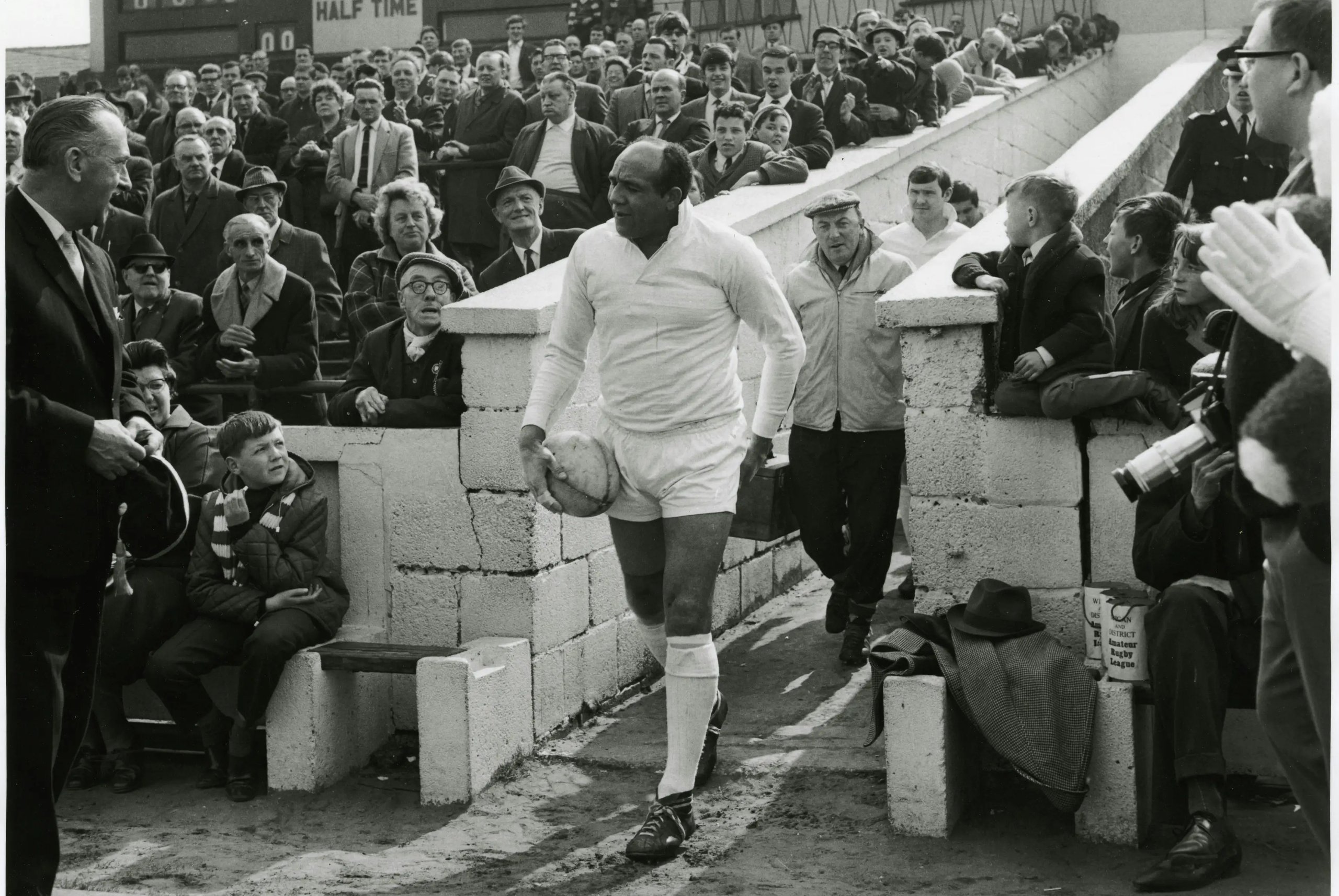 Rugby player walks with ball during his last match, crowds watch.