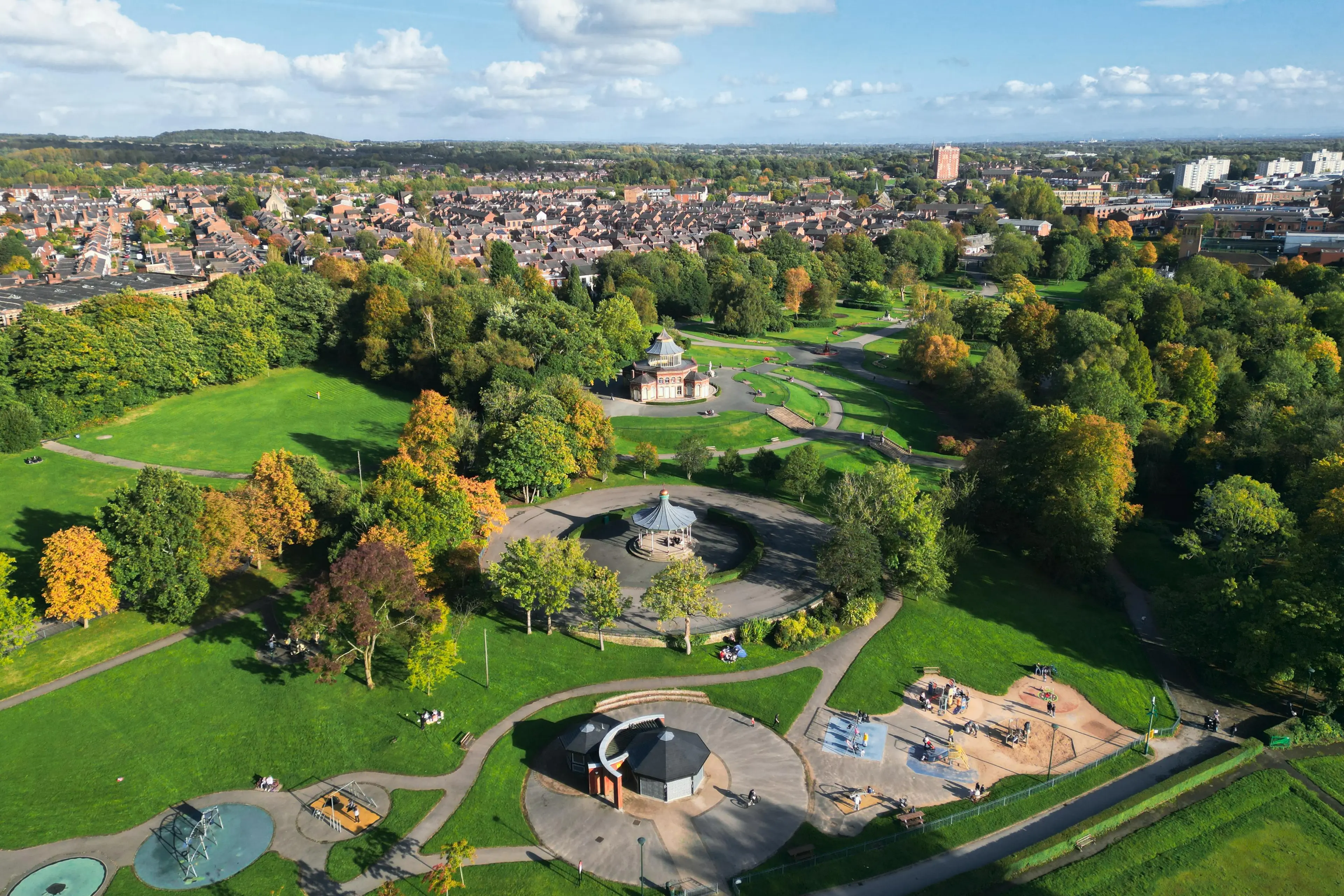 Aerial view of Mesnes Park with town in the background, blue sky.