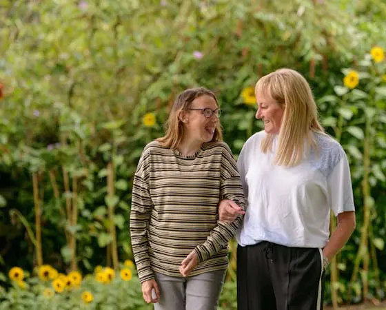 Women arm in arm, laughing, in a sunny garden.