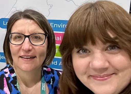 Two women smiling, Team Wigan backdrop.
