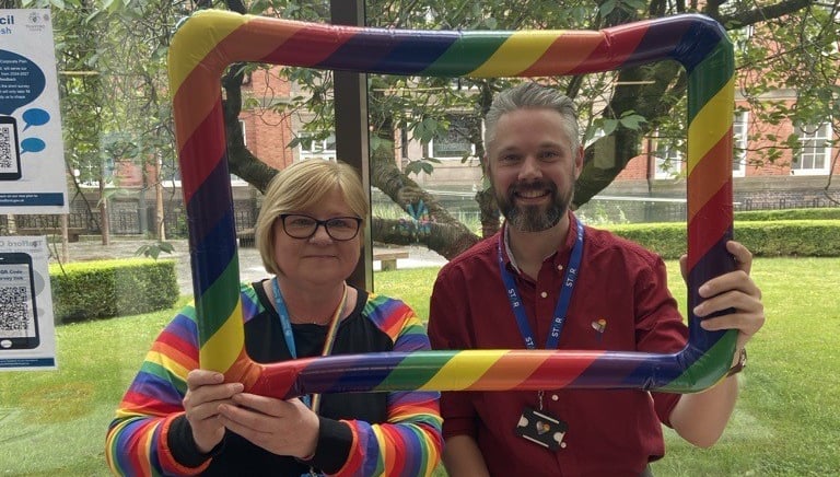 Two people posing with rainbow frame.