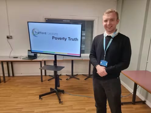 Man standing by a screen; "Poverty Truth" displayed.