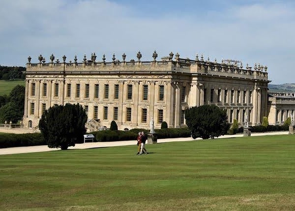 Large manor, green lawn, trees, and cloudy blue sky.
