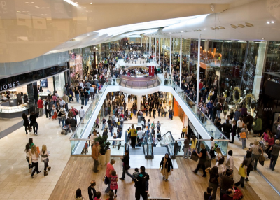 People in a large, modern shopping mall with escalators and multiple levels.