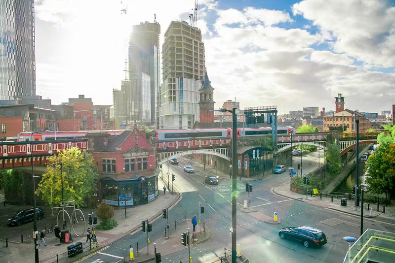 Buildings, train, and road in a city under a cloudy sky.