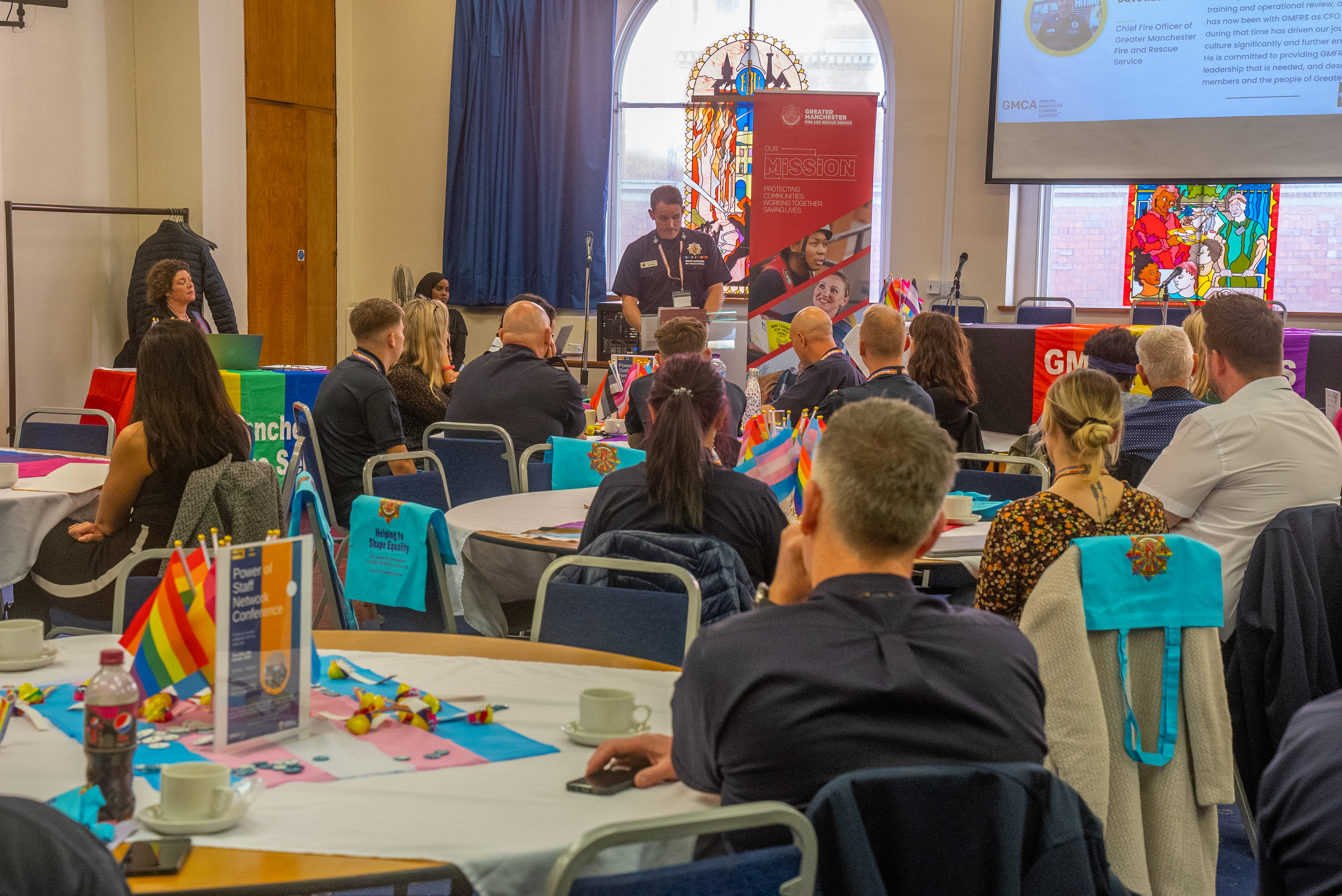 People seated at tables in a conference room with flags.
