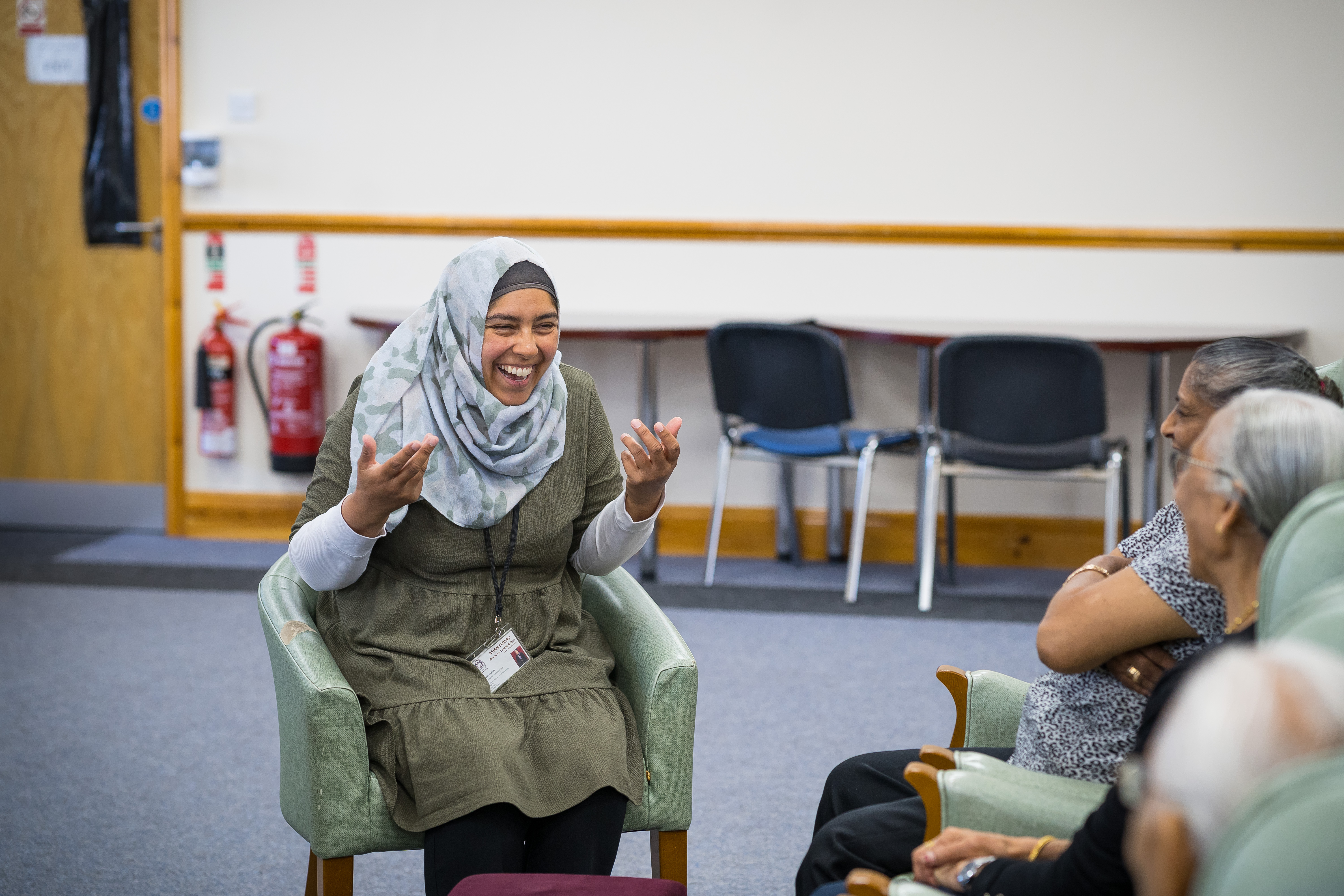 People in care home sitting and smiling. Woman wearing hijab talking.