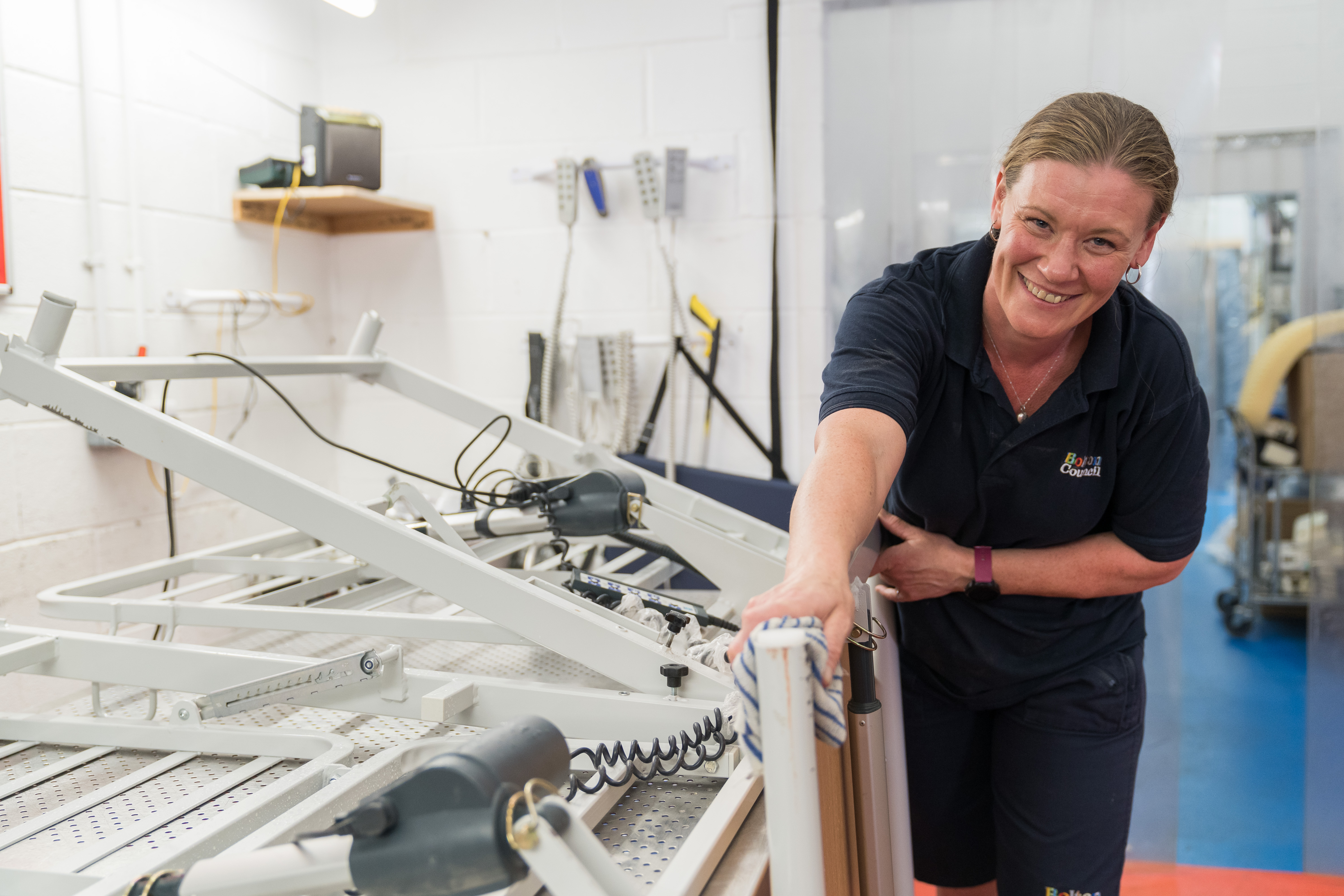 Smiling staff member next to a bed frame. They are touching the frame.