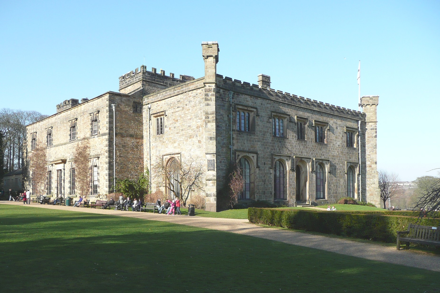 Large stone building, people on benches, green grass.