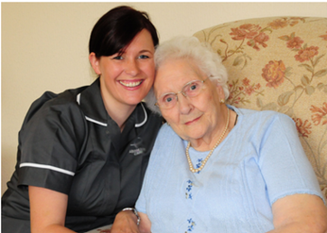 Caregiver with elderly woman, smiling, sitting.