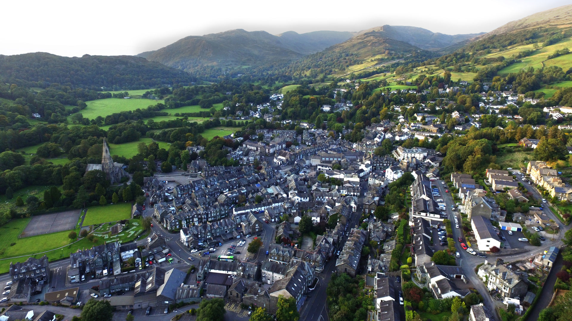 Aerial view of the town of Ambleside, with a church and green hills in the background.