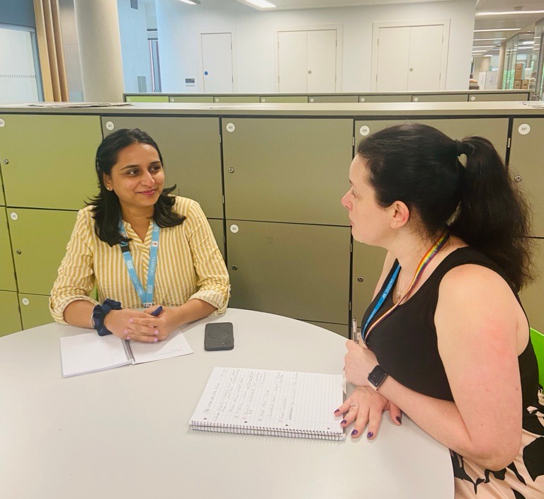 Two women sitting at a table in a meeting, with notebooks.