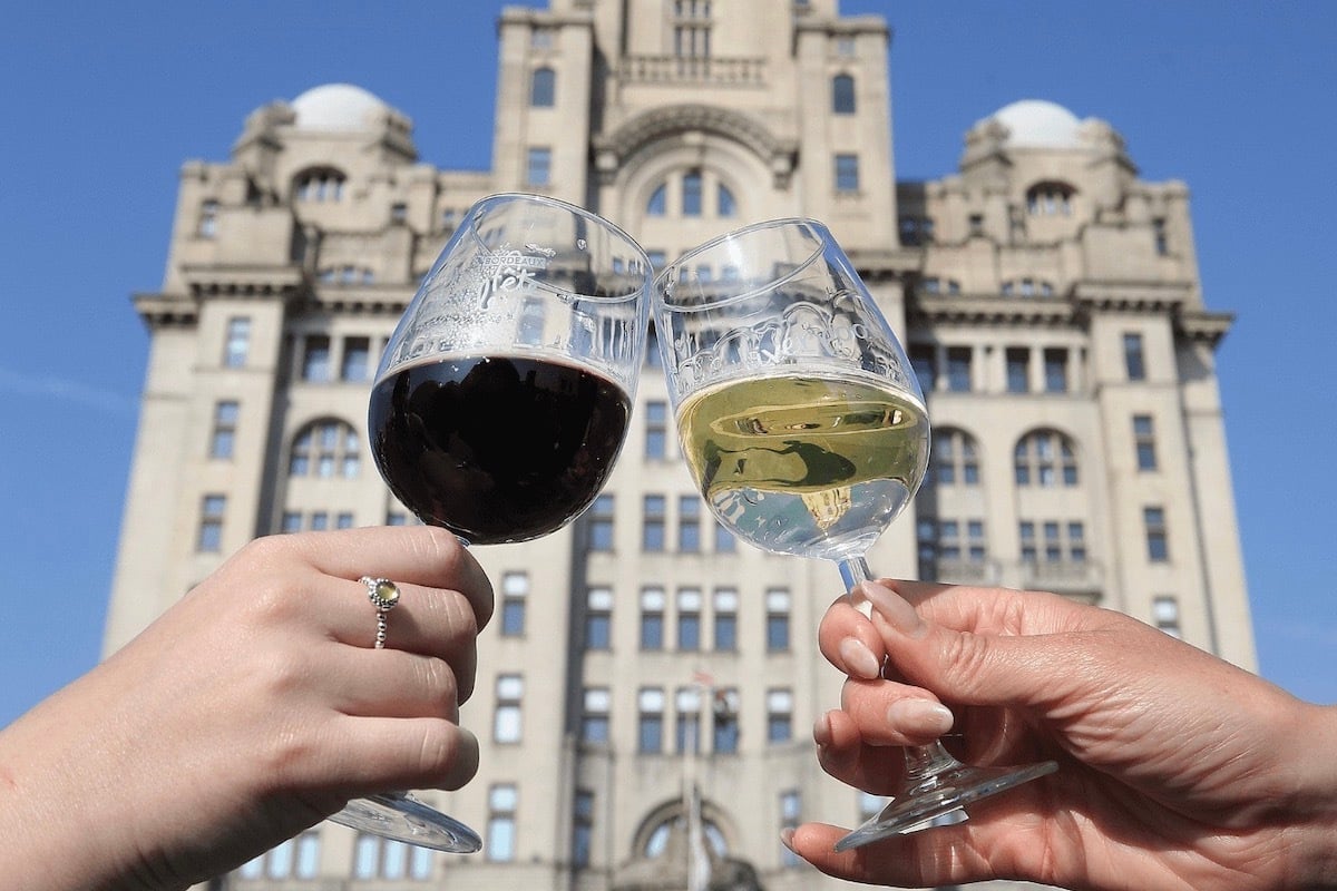 Two wine glasses clink in front of a building. One has red wine, the other white.