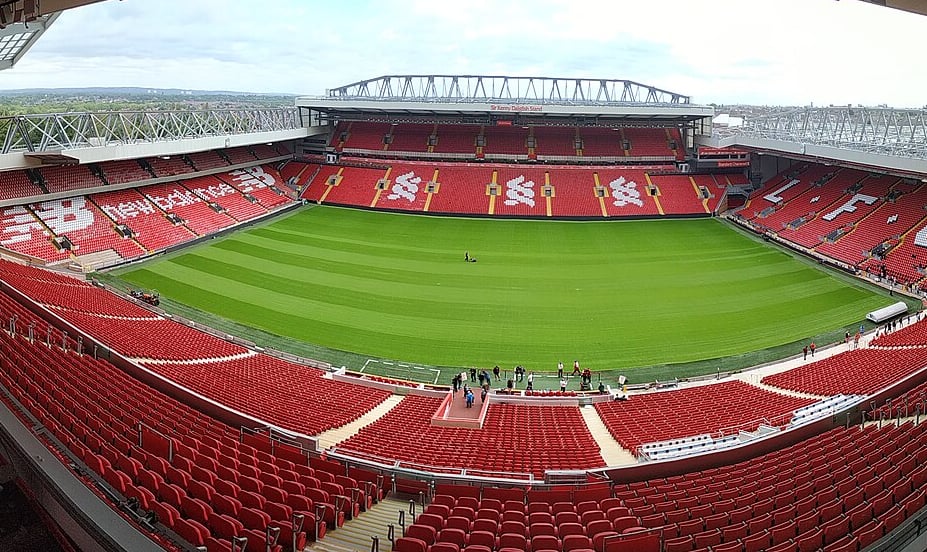 View of Anfield stadium with red seats, green pitch, and New Balance logo.