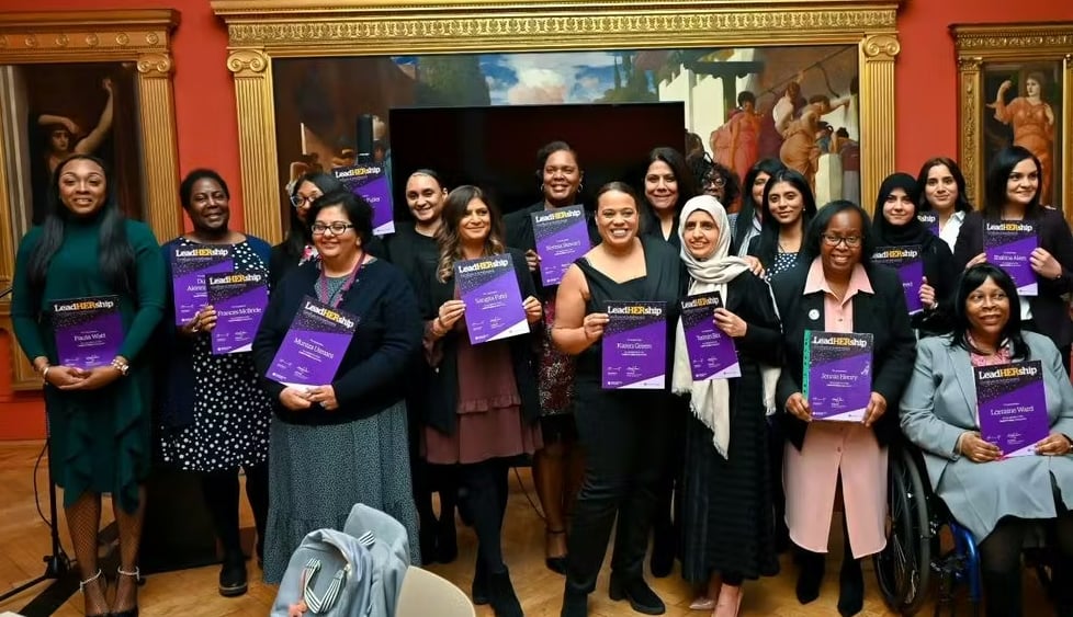 Group of women smiling and holding certificates after completing the LeadHership program, standing together in a formal setting with a classical painting in the background.