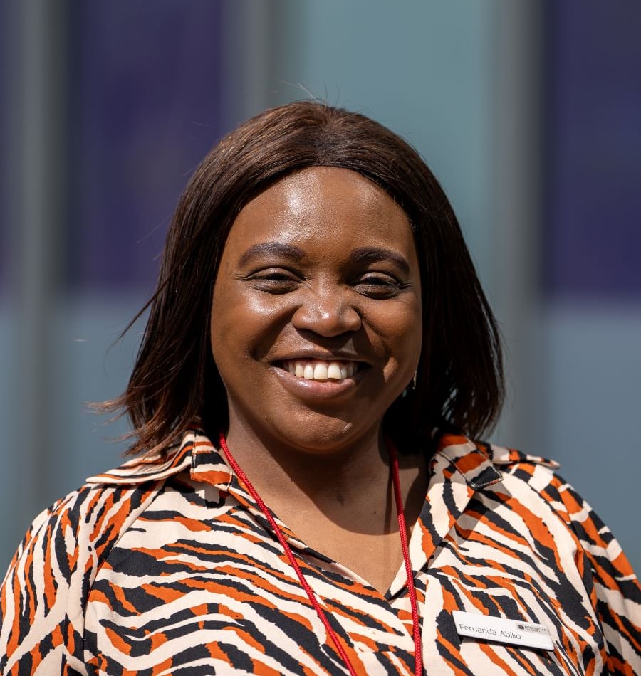 Woman with brown hair smiling, wearing a patterned shirt and lanyard.