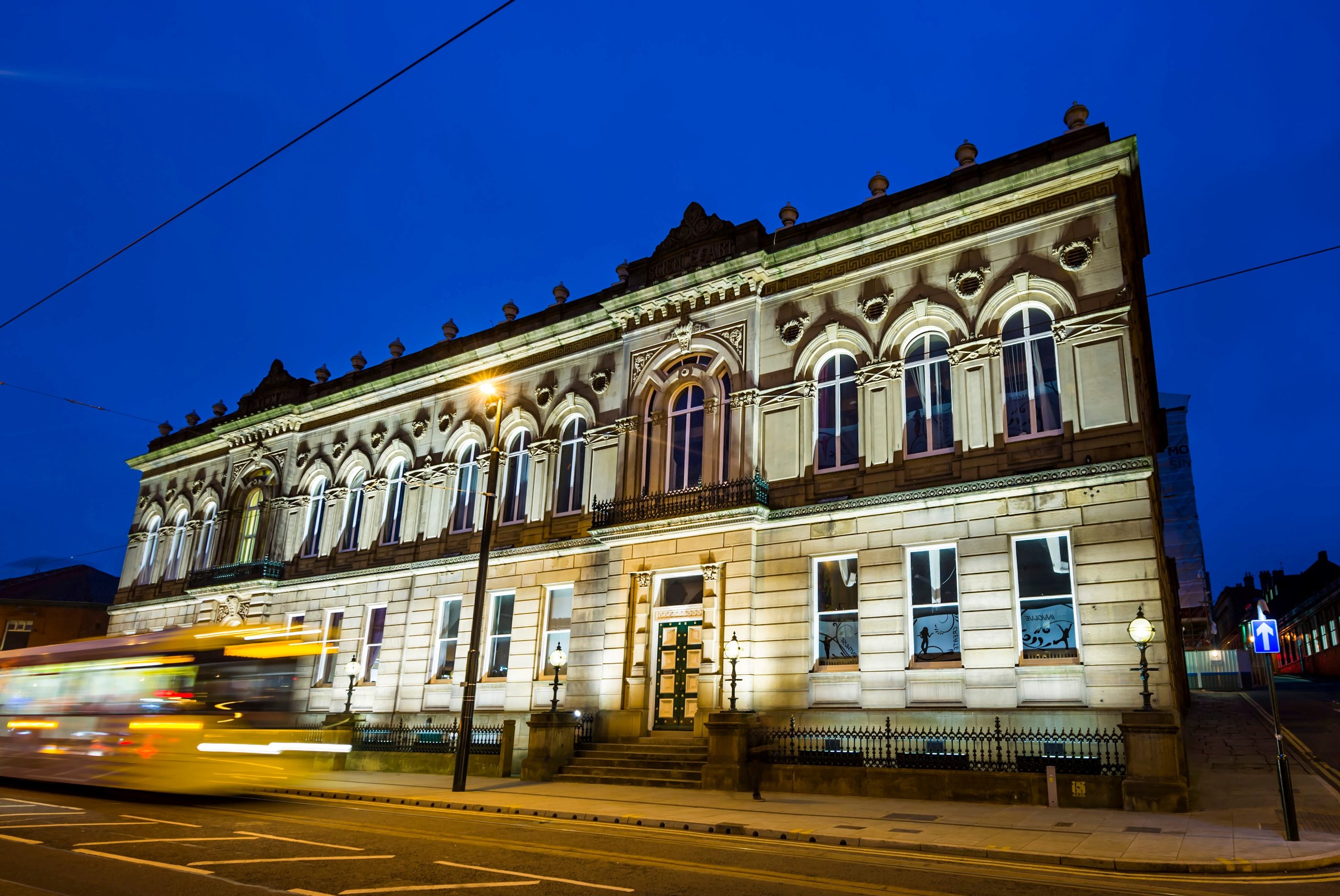 A building illuminated at night with a blurred bus passing by.