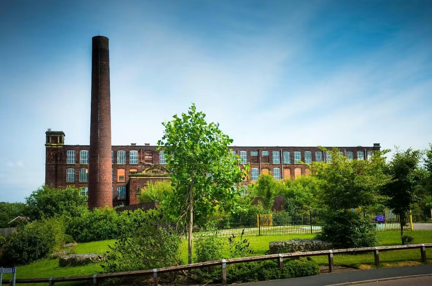 Old brick mill with tall chimney against a blue sky.