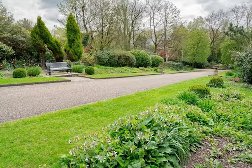 Path in a park with grass, trees, and a bench.