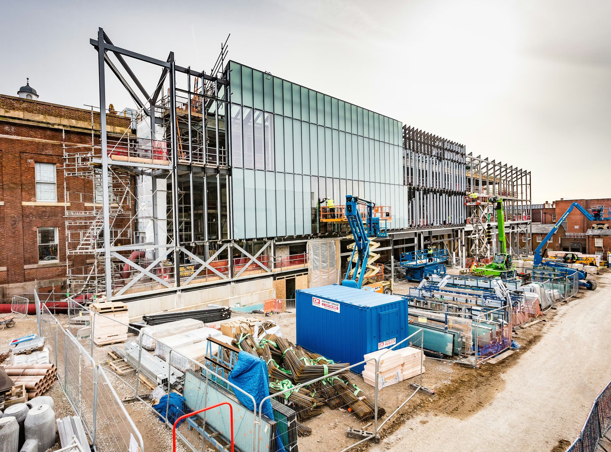 Modern building under construction with cranes, scaffolding, and materials.