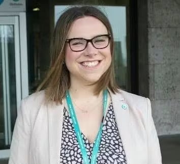 Smiling woman with glasses, blazer, and a lanyard.