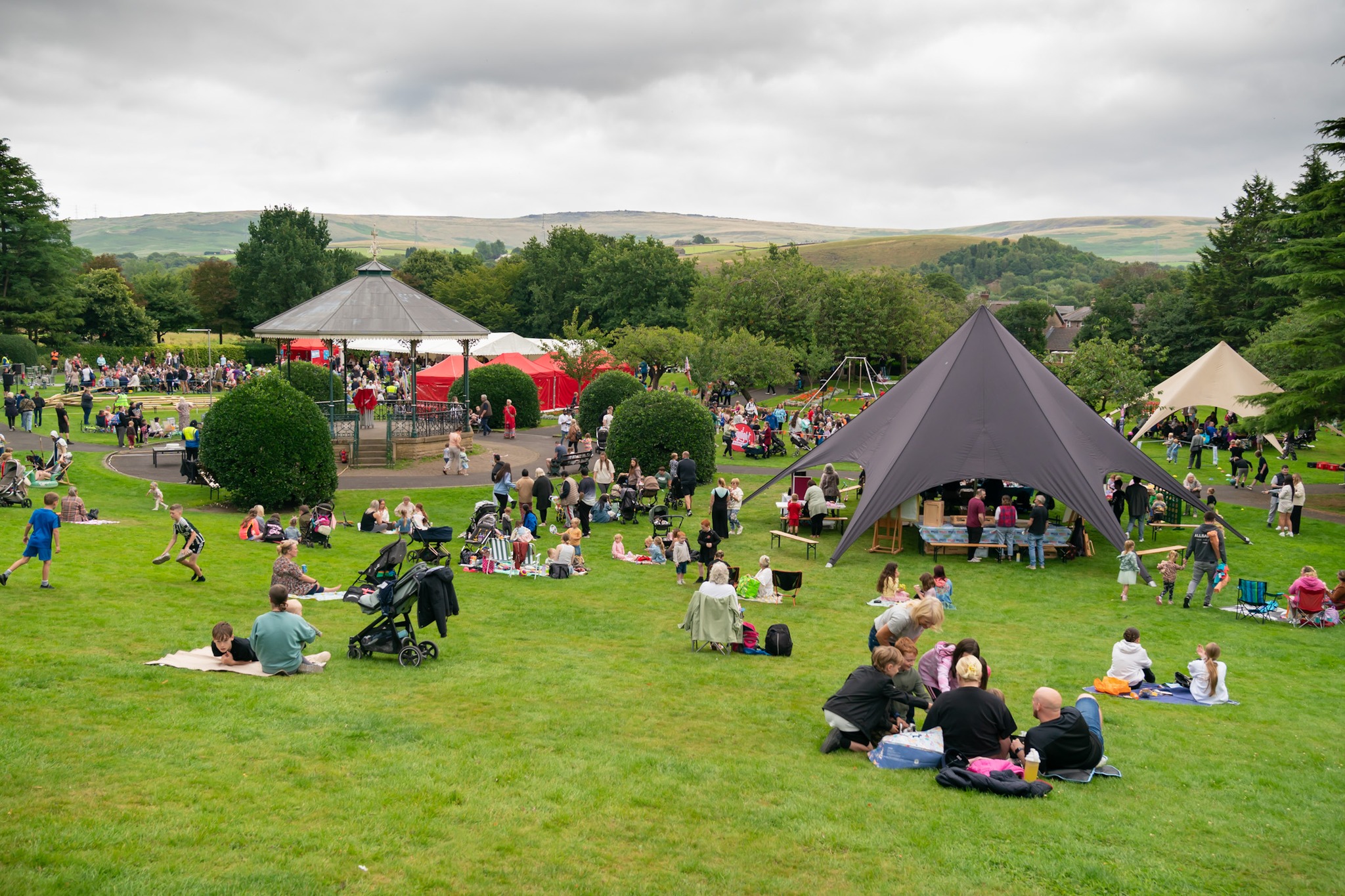 People enjoying a picnic on a grassy field with tents and a gazebo.